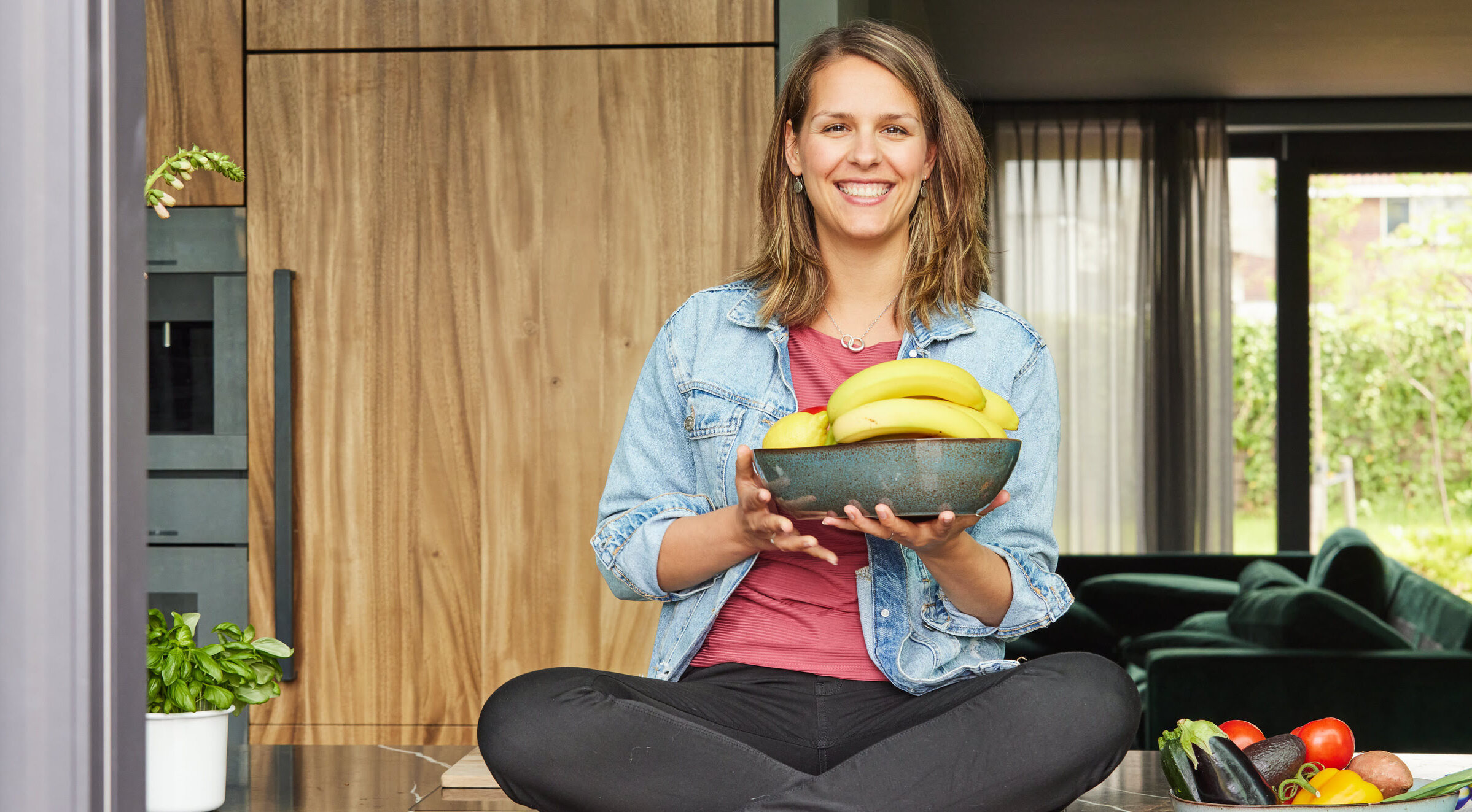 Rebecca Fruwert - Vegan diet coach sitting on a table holding a bowl of fruits in her hands